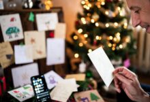 Cozy holiday scene with cards, smartphone, and a person holding a warm holiday message.