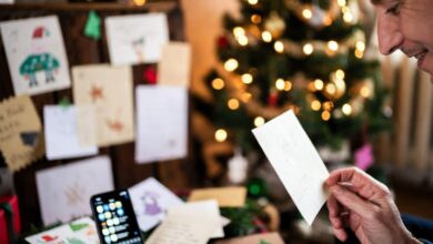 Cozy holiday scene with cards, smartphone, and a person holding a warm holiday message.