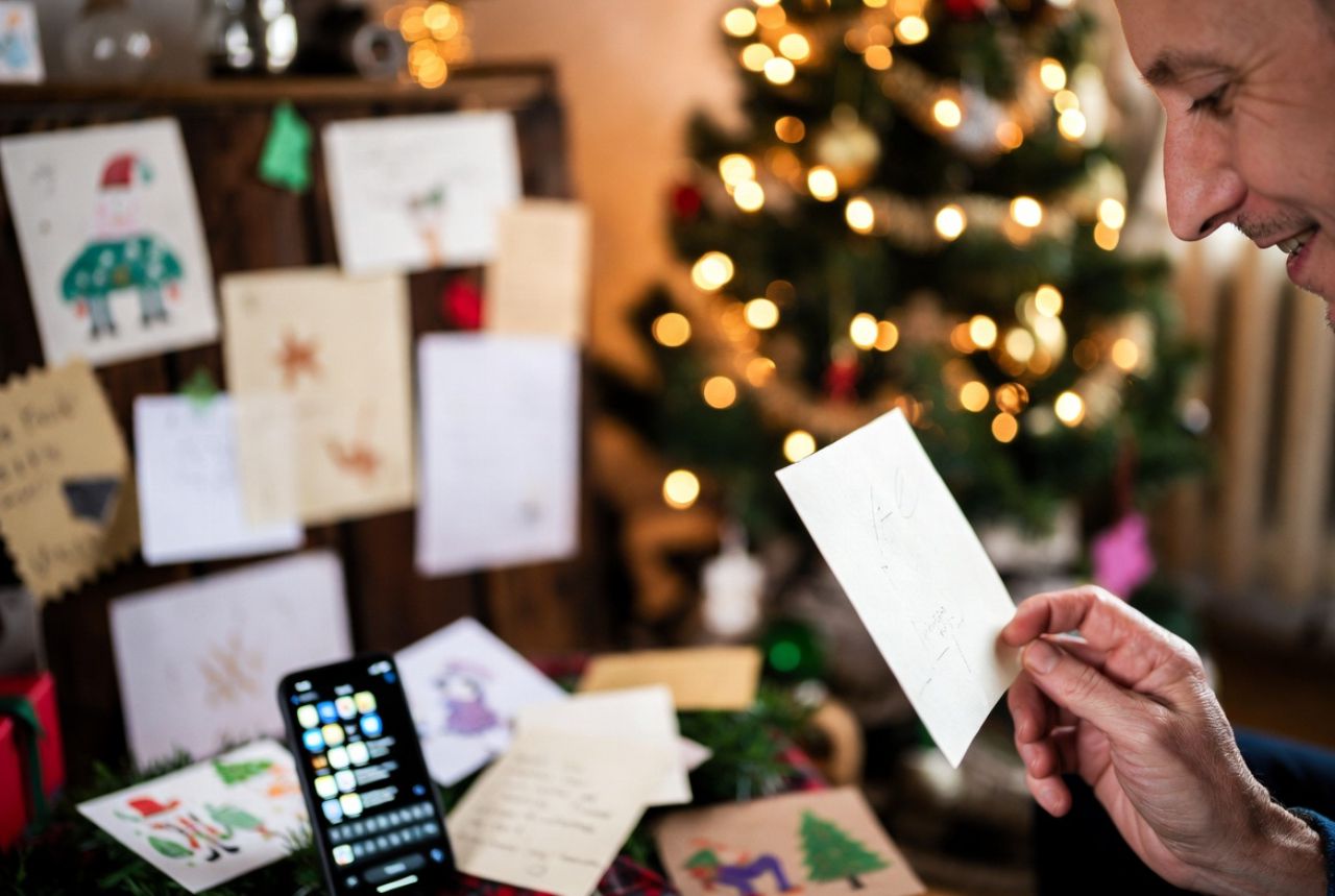 Cozy holiday scene with cards, smartphone, and a person holding a warm holiday message.
