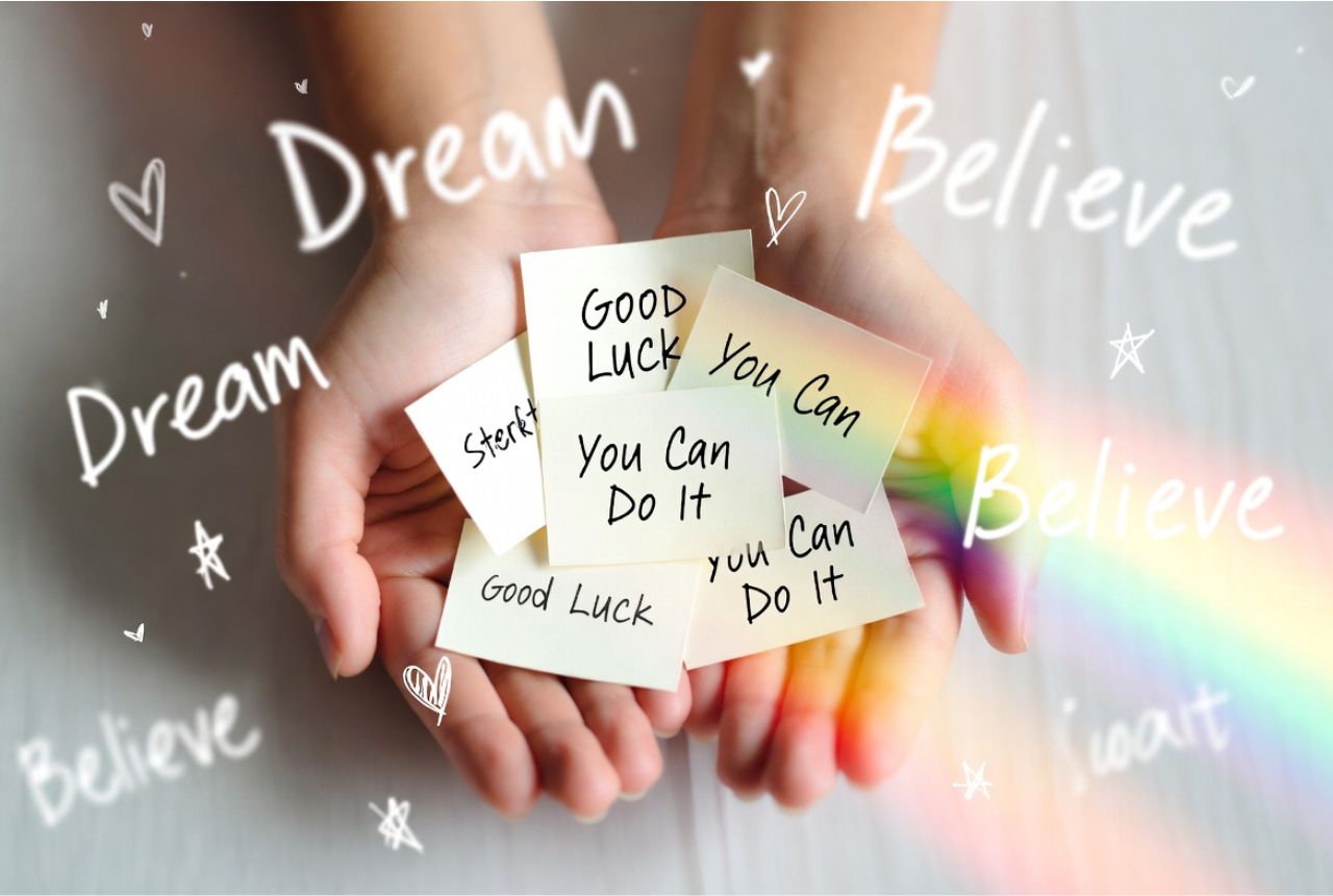 “Hands holding handwritten good luck cards surrounded by glowing light and motivational symbols like hearts and stars.”