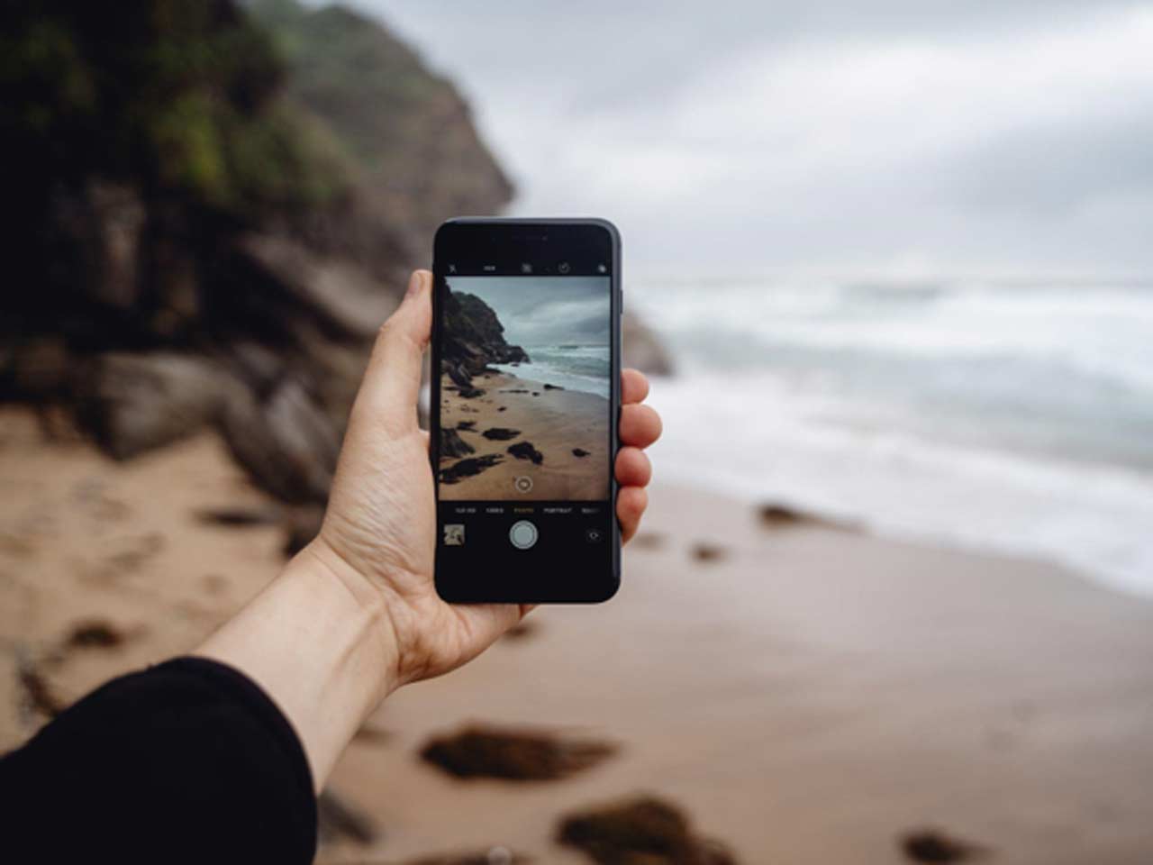 Hand holding a smartphone to photograph a rocky beach